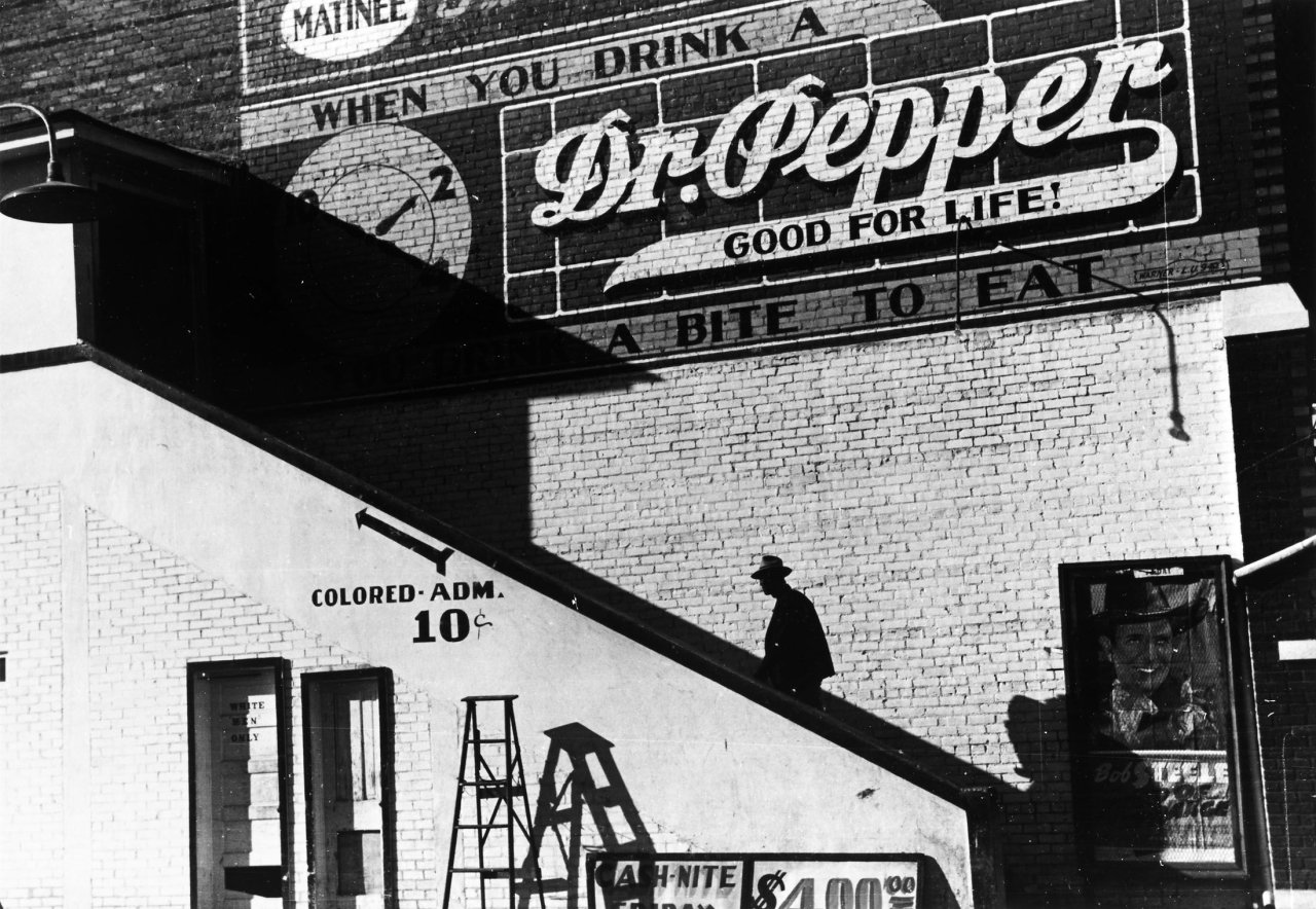 Auf diesem Bild ist das folgende Kunstwerk zu sehen: Marion Post Wolcott. Negro going in colored entrance of movie house on Saturday afternoon, Belzoni, Mississippi Delta. 1939.