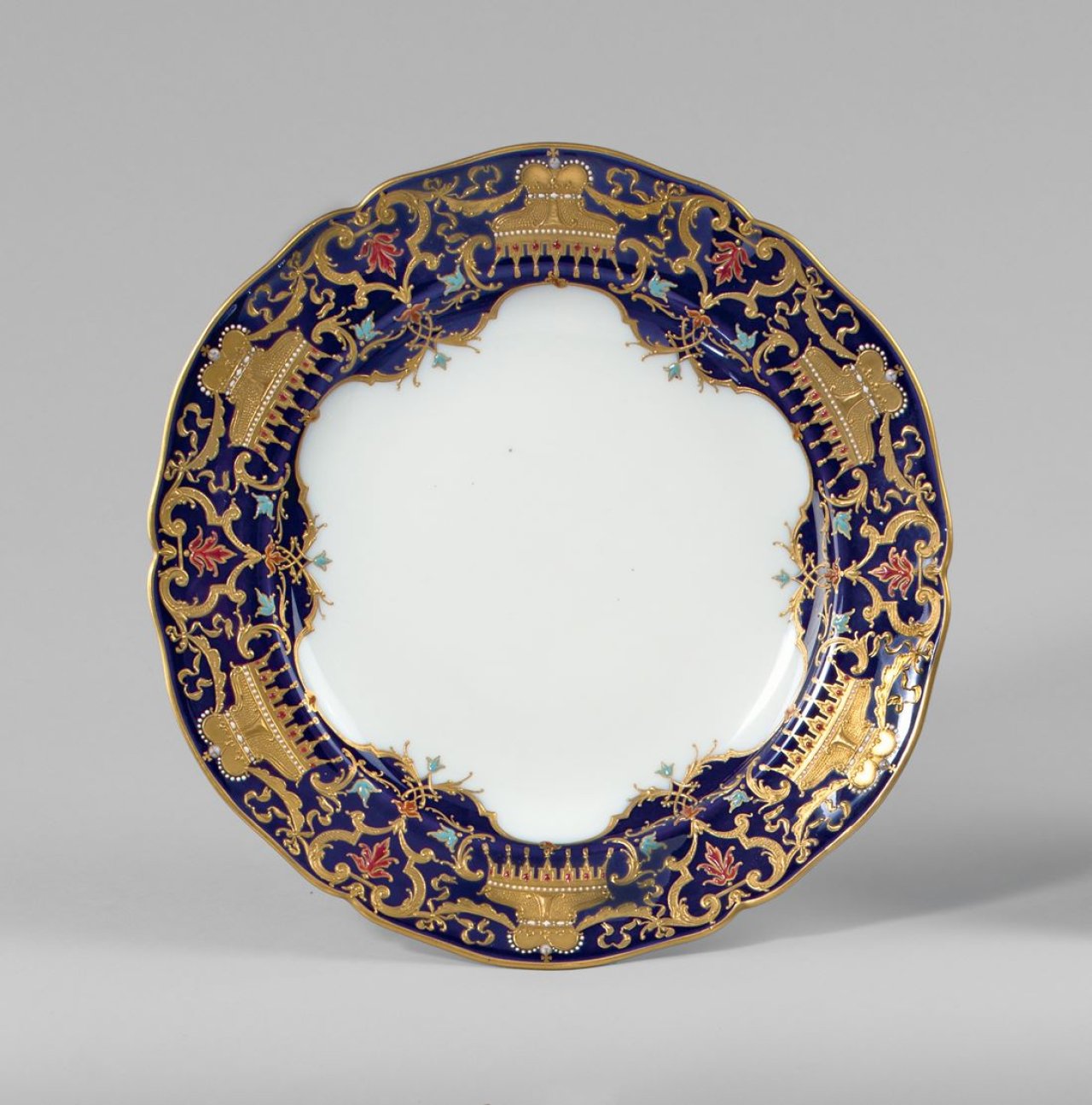 Auf diesem Bild ist das folgende Kunstwerk zu sehen:  KPM Königliche Porzellan-Manufaktur Berlin. Zierteller Englischglatt mit Fürstenhüten in Reliefgold und Emaillemalerei auf blauem Fond. Um 1900/10.