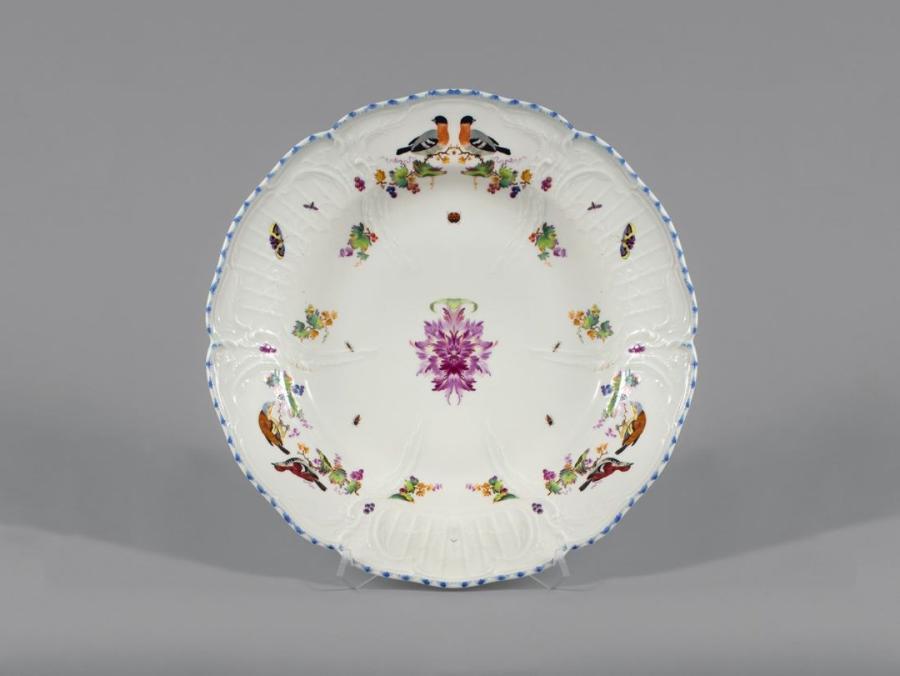 Auf diesem Bild ist das folgende Kunstwerk zu sehen:  KPM Königliche Porzellan-Manufaktur Berlin. Runde Platte aus dem Tafelservice für Friedrich Ehrenreich von Ramin (1709–1782), Geschenk von König Friedrich dem Großen – Reliefzierat mit farbiger Blumen- und Vogelmalerei und blau angespitztem Rand. 1768.