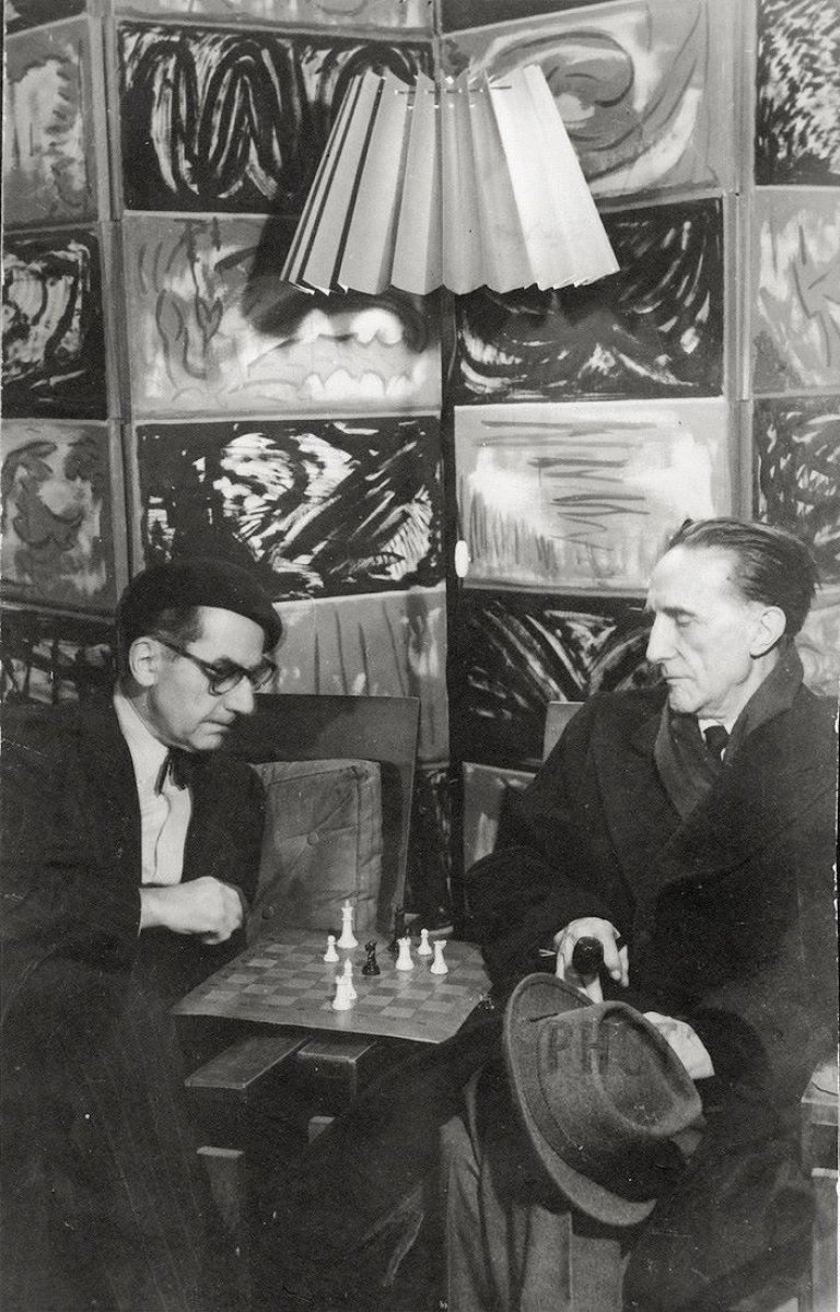 Auf diesem Bild ist das folgende Kunstwerk zu sehen:  Man Ray. Man Ray und Marcel Duchamp beim Schach in Man Rays Atelier in der Rue Férou, Paris. 1960.