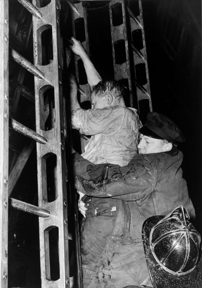 Auf diesem Bild ist das folgende Kunstwerk zu sehen:  Weegee (d.i. Fellig, Arthur H.). Fireman helping man down a ladder. Um 1940.
