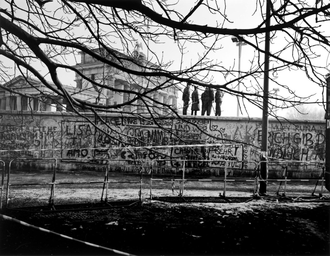 Auf diesem Bild ist das folgende Kunstwerk zu sehen: Thomas Lüttge. „Vier auf der Mauer“, Berlin, Brandenburger Tor, Dezember. 1989.