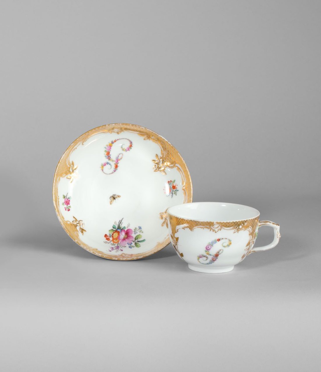 Auf diesem Bild ist das folgende Kunstwerk zu sehen:  KPM Königliche Porzellan-Manufaktur Berlin. Tasse und Untertasse Neuzierat mit farbigen Blumenbuchstaben G und Goldschuppenmosaik. Um 1780.