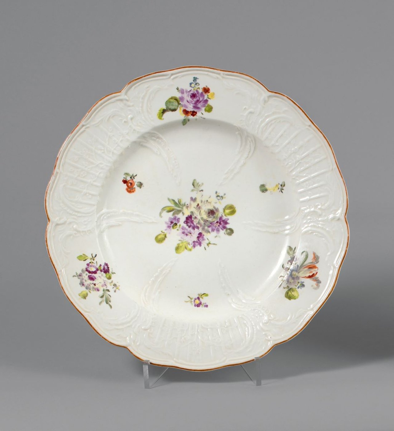 Auf diesem Bild ist das folgende Kunstwerk zu sehen:  KPM Königliche Porzellan-Manufaktur Berlin. Teller aus dem Tafelservice für den Bruder Friedrichs des Großen, Prinz Heinrich von Preußen (1726–1802), Reliefzierat mit braunorangem Rand und Blumenmalerei. für das Schloß Rheinsberg. Um 1764/65.