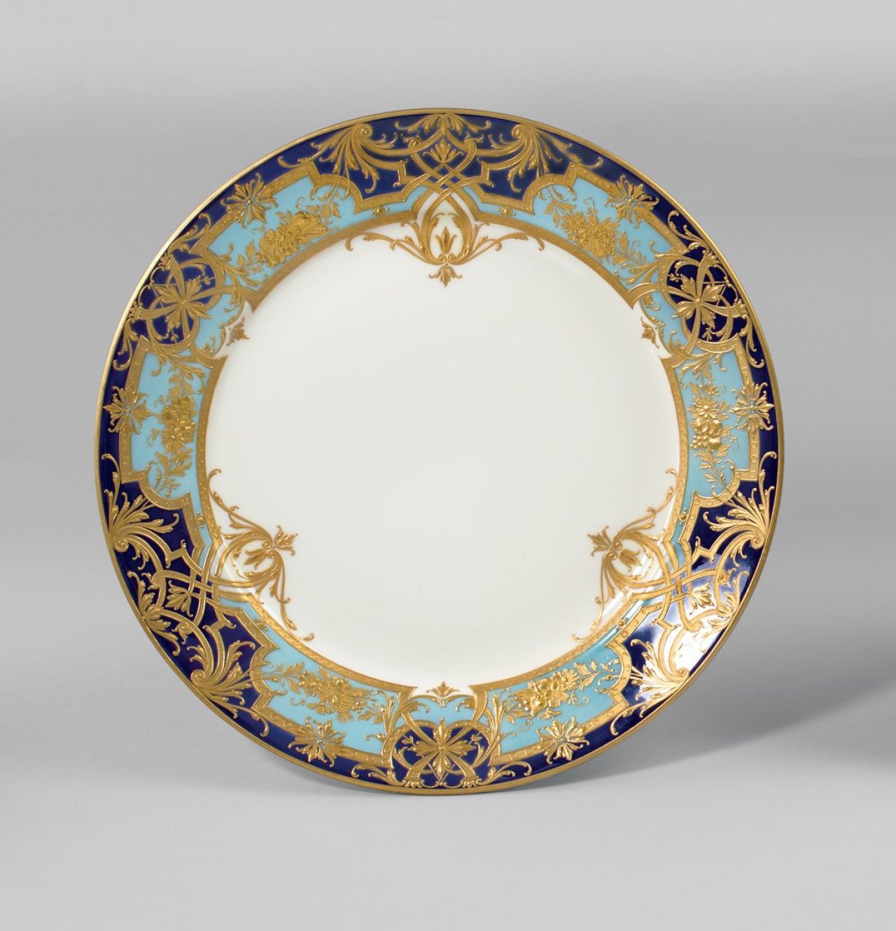 Auf diesem Bild ist das folgende Kunstwerk zu sehen:  KPM Königliche Porzellan-Manufaktur Berlin. Zierteller Rheinische Form mit Bandelwerk in Reliefgold auf blauem und hellblauem Fond. Um 1900/10.