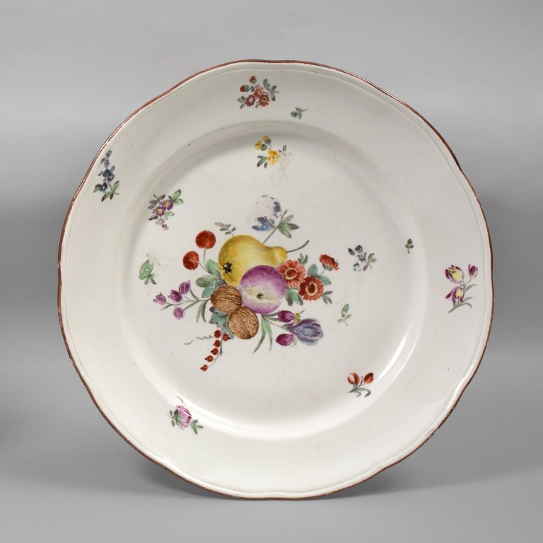 Auf diesem Bild ist das folgende Kunstwerk zu sehen:  Porzellanmanufaktur Frankenthal. Teller mit Früchten, Streublumen und braunem Rand. 1781.