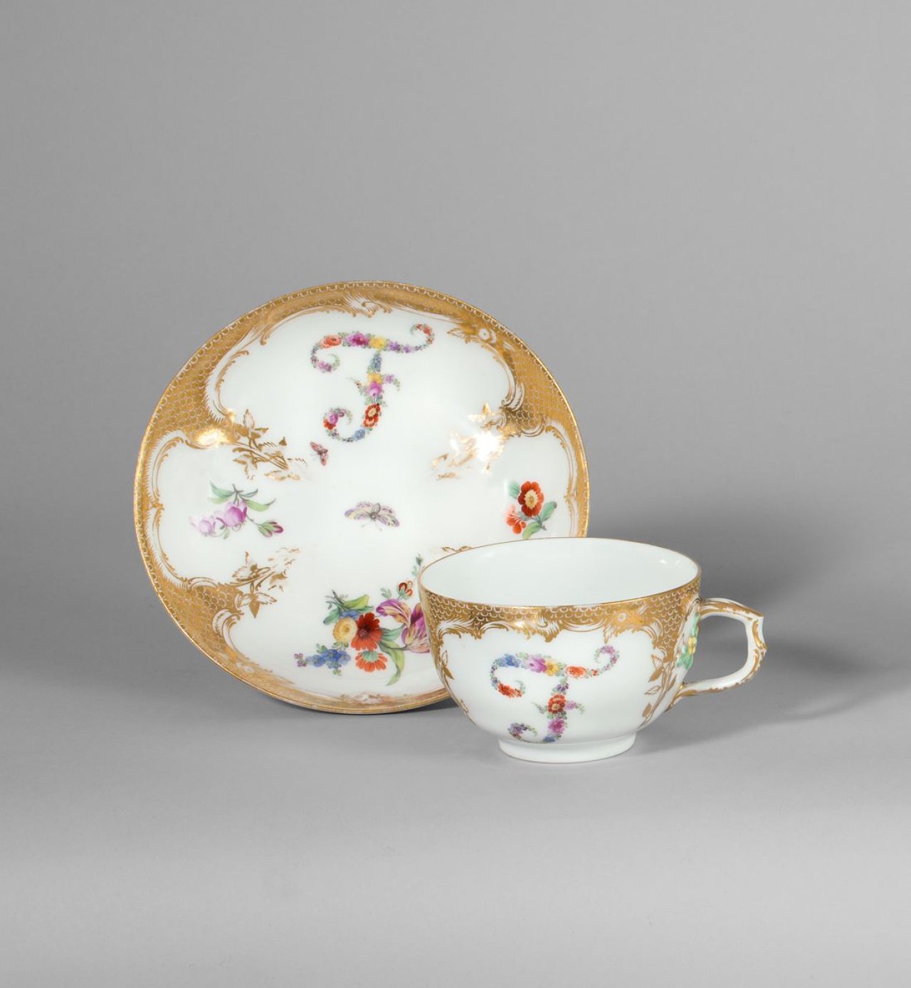 Auf diesem Bild ist das folgende Kunstwerk zu sehen:  KPM Königliche Porzellan-Manufaktur Berlin. Tasse und Untertasse Neuzierat mit farbigen Blumenbuchstaben F und Goldschuppenmosaik. Um 1775.