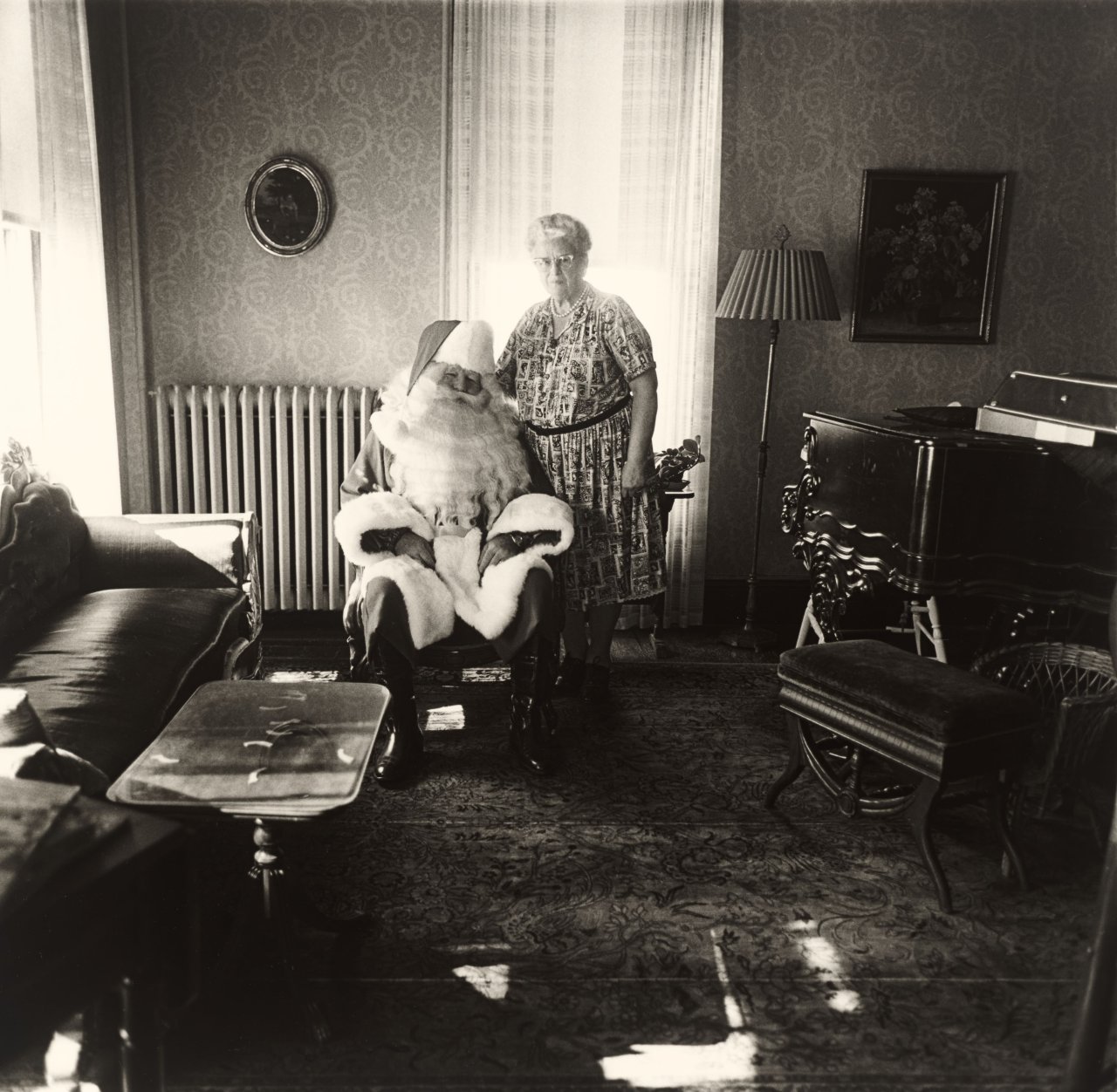 This picture shows the following artwork: Diane Arbus. Mr. and Mrs. Santa Claus in their living room, Albion, N.Y. 1964.