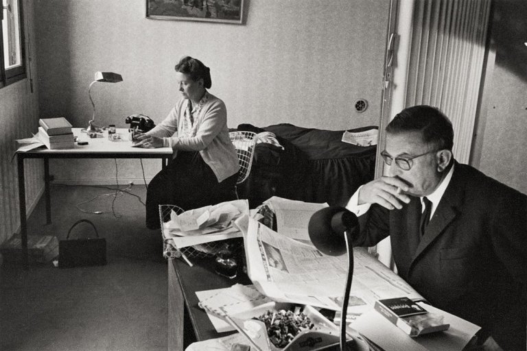 Auf diesem Bild ist das folgende Kunstwerk zu sehen: Gisèle Freund. Jean-Paul Sartre und Simone de Beauvoir bei der Arbeit, Boulevard Raspail 222, Paris. 1964.