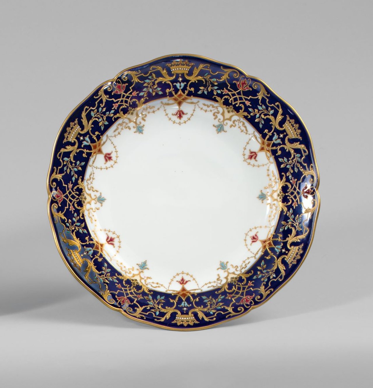 Auf diesem Bild ist das folgende Kunstwerk zu sehen:  KPM Königliche Porzellan-Manufaktur Berlin. Zierteller Englischglatt mit Grafenkronen in Reliefgold und Emailemalerei auf blauem Fond. Um 1900/10.