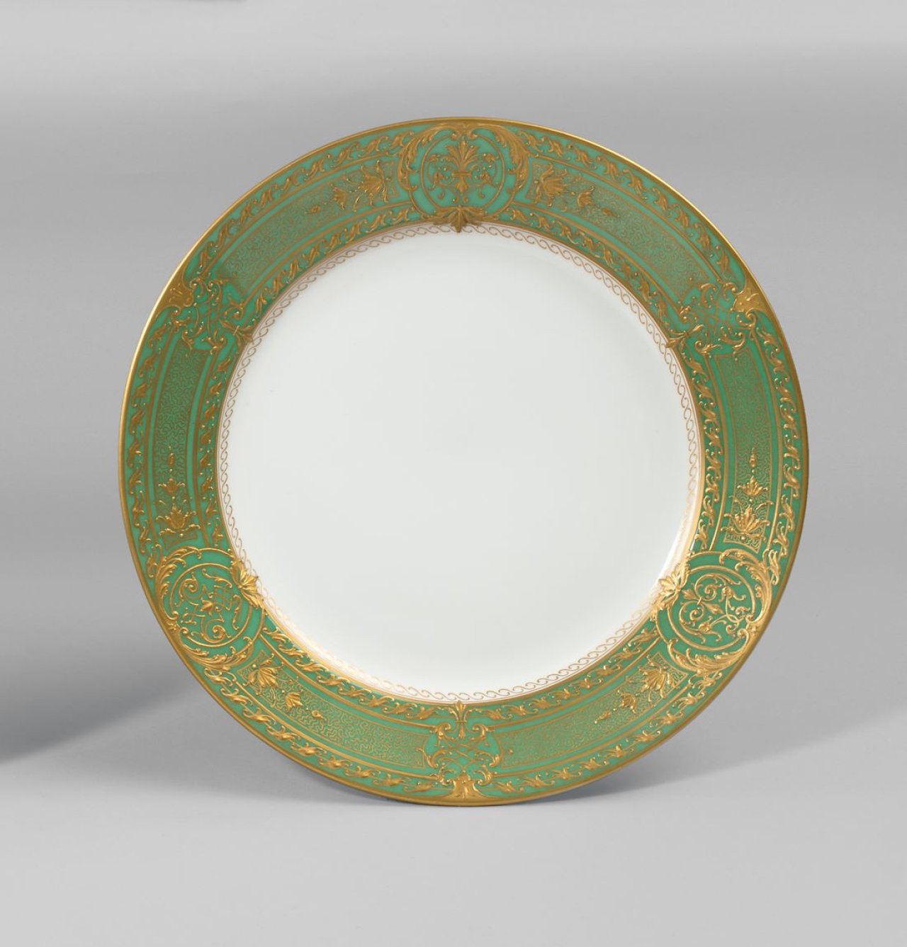 Auf diesem Bild ist das folgende Kunstwerk zu sehen:  KPM Königliche Porzellan-Manufaktur Berlin. Zierteller Rheinische Form mit Régenceornamenten und Vermicelliband in Reliefgold auf grünem Fond. 1914–18.