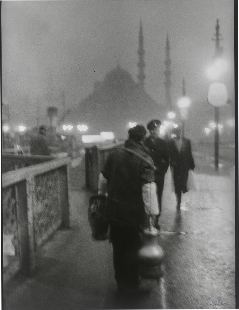 Auf diesem Bild ist das folgende Kunstwerk zu sehen: Ara Güler. 'Salep' Seller in early morning light on the old Galata Bridge. 1957.