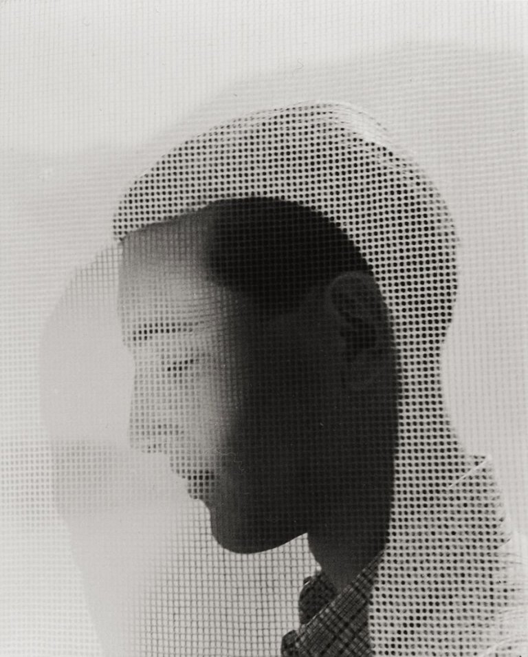 Auf diesem Bild ist das folgende Kunstwerk zu sehen: Herbert List. Junger Mann hinter einer Gardine. Um 1937.