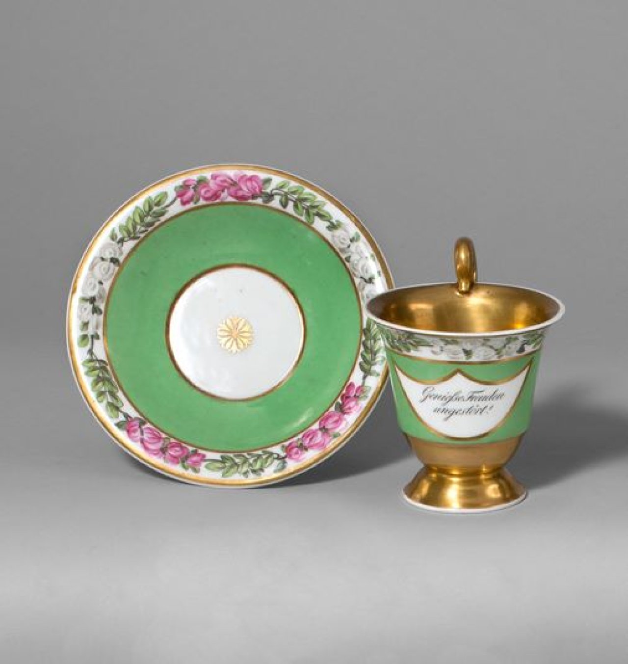 Auf diesem Bild ist das folgende Kunstwerk zu sehen:  KPM Königliche Porzellan-Manufaktur Berlin. Gedenktasse Glockenbecherform mit Rosettenhenkel und dem Sinnspruch „Genieße Freuden ungestört“ auf grünem Fond, Blumenband und reicher Vergoldung. Um 1820.