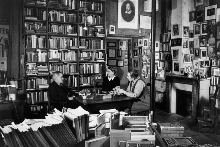 Auf diesem Bild ist das folgende Kunstwerk zu sehen: Gisèle Freund. „James Joyce in Sylvia Beach's bookshop „Shakespeare & Co“, rue de l'Odéon, with Sylvia Beach and Adrienne Monnier, his publishers in English and French of 'Ulysse'“. 1938.