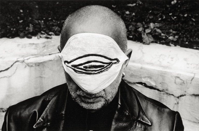 Auf diesem Bild ist das folgende Kunstwerk zu sehen: Stefan Moses. „Jörg Immendorf mit Muttermundmaske“, aus der Serie „Künstler machen Masken“. 1997.