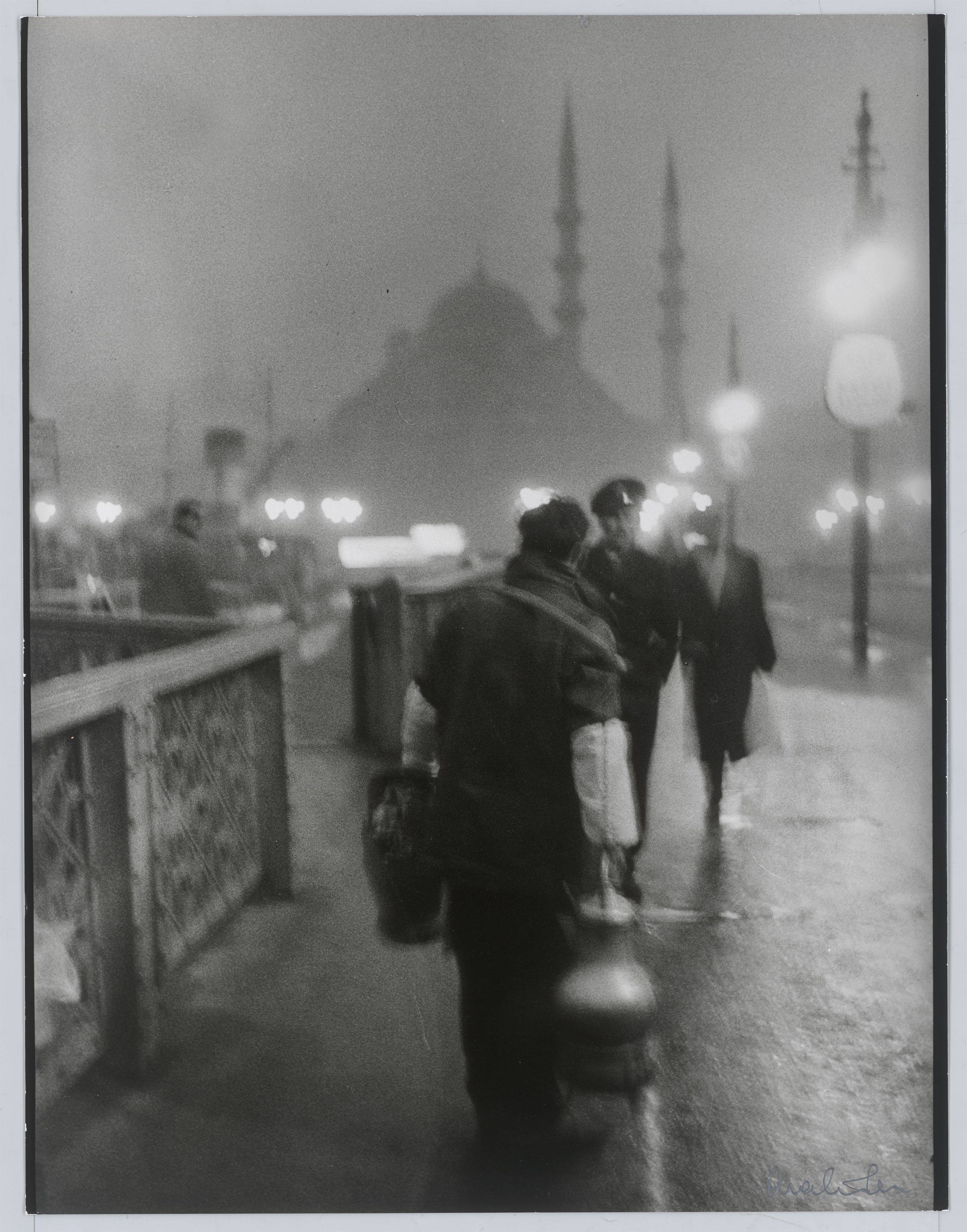 This picture shows the following artwork: Ara Güler. 'Salep' Seller in early morning light on the old Galata Bridge. 1957.