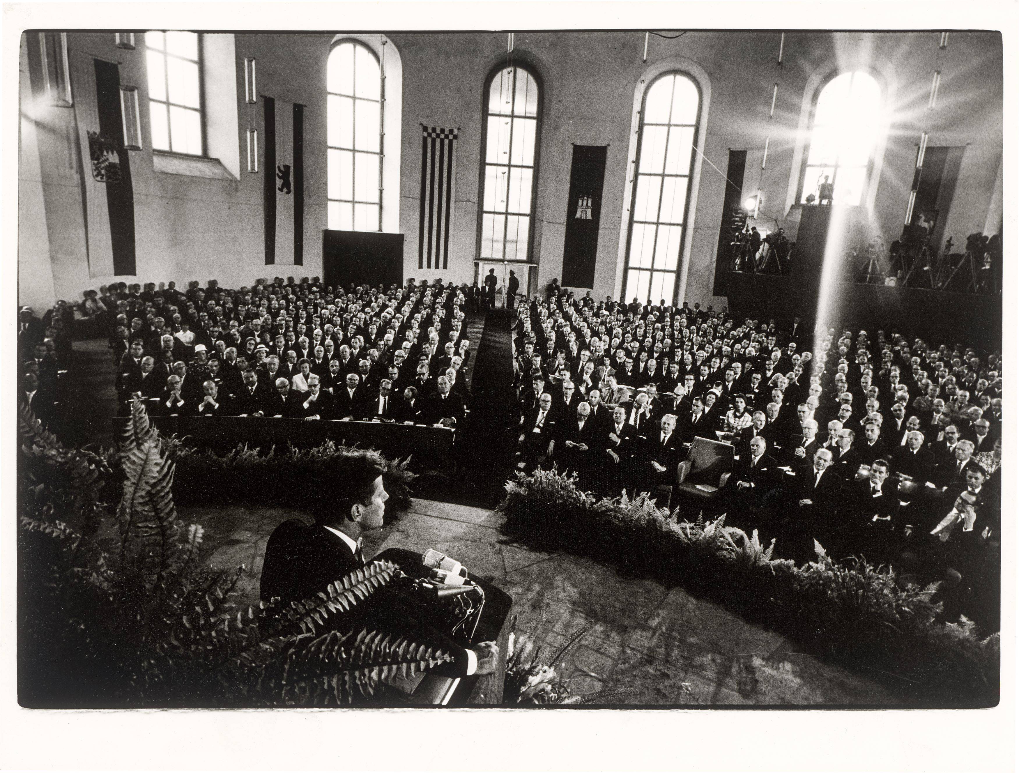 Auf diesem Bild ist das folgende Kunstwerk zu sehen: Will McBride. „John F. Kennedy spricht in der Paulskirche, Frankfurt am Main“. 1963.