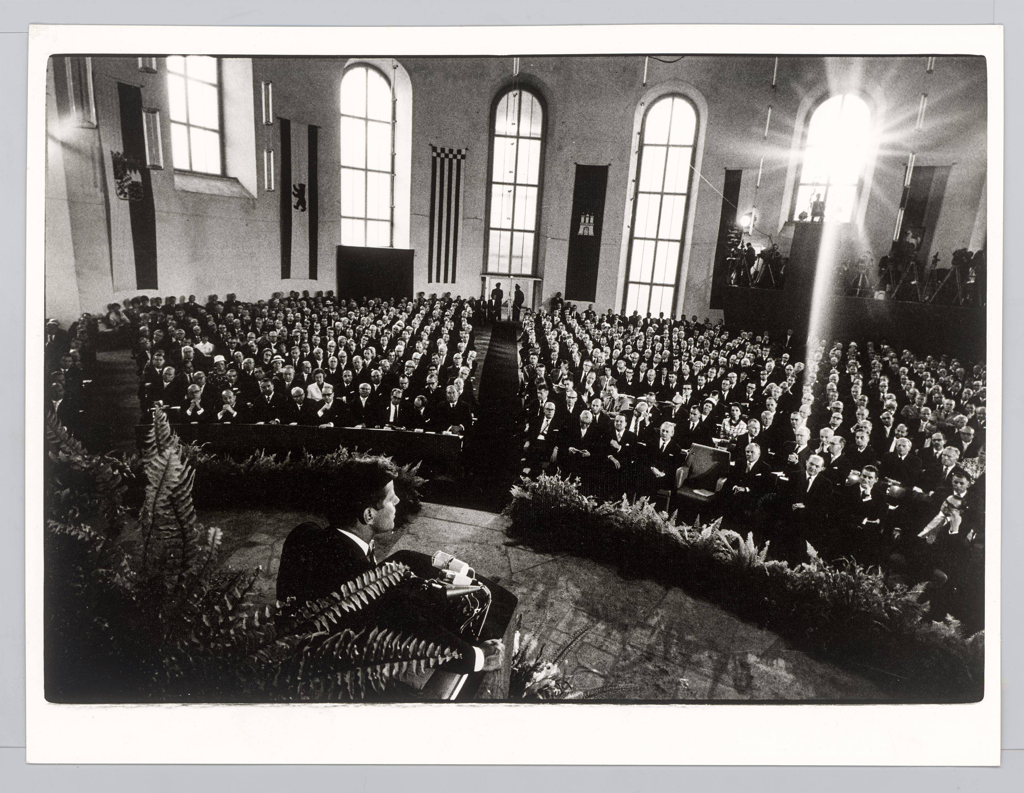 Auf diesem Bild ist das folgende Kunstwerk zu sehen: Will McBride. „John F. Kennedy spricht in der Paulskirche, Frankfurt am Main“. 1963.