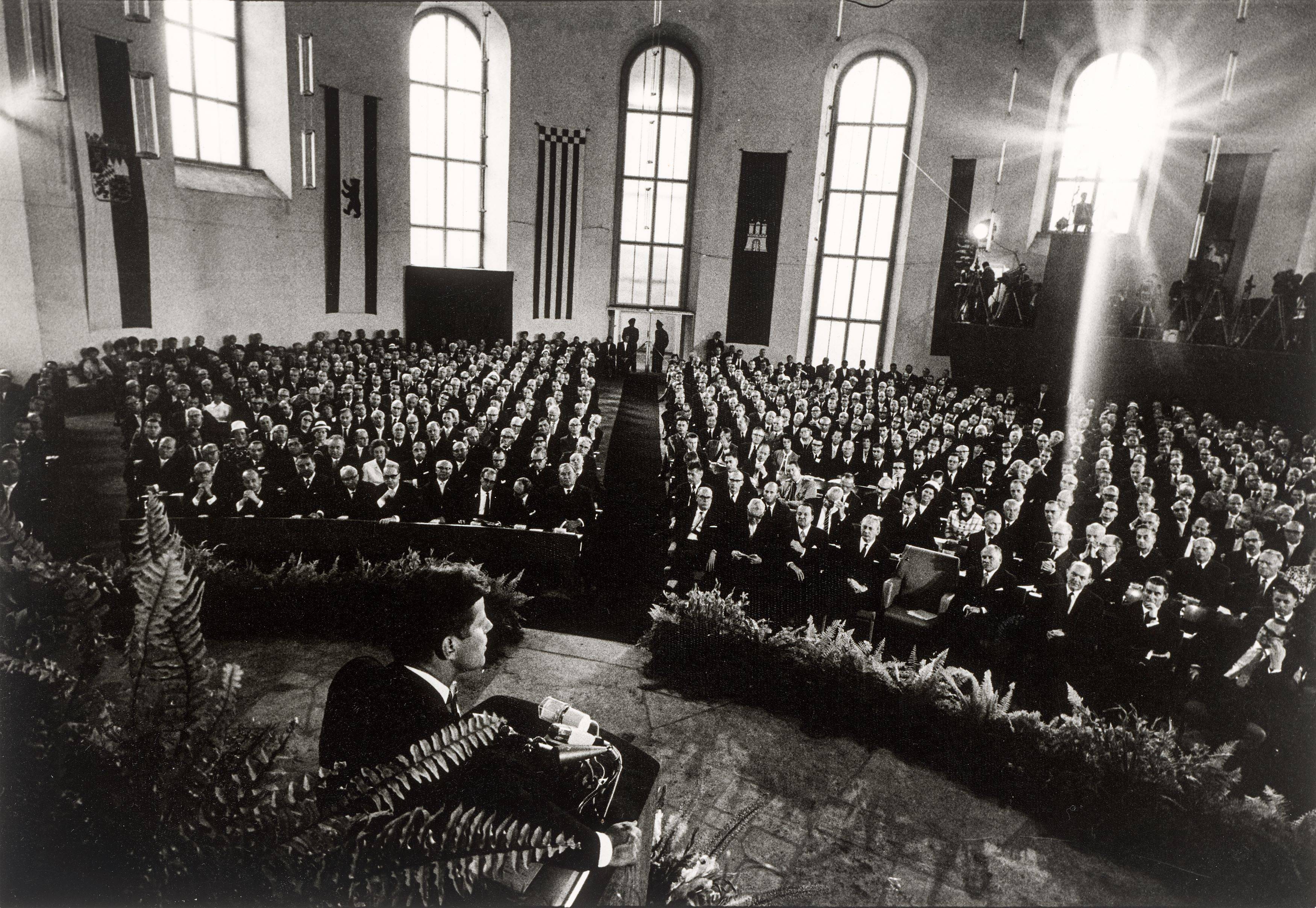 Auf diesem Bild ist das folgende Kunstwerk zu sehen: Will McBride. „John F. Kennedy spricht in der Paulskirche, Frankfurt am Main“. 1963.
