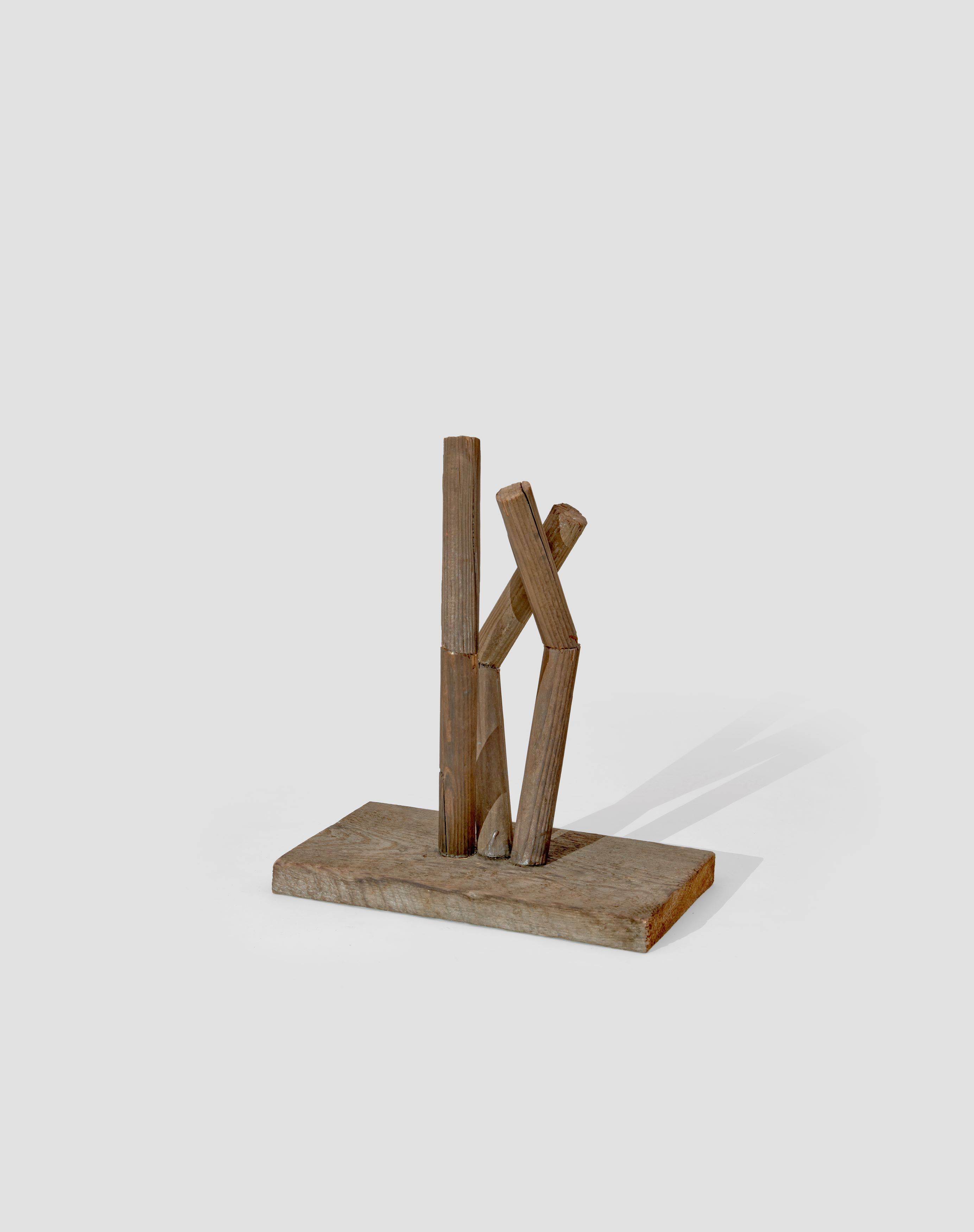 Auf diesem Bild ist das folgende Kunstwerk zu sehen: Hermann Glöckner. Aufrichtung von drei geteilten und gewinkelten Rundhölzern auf Holzplinthe. 1978.